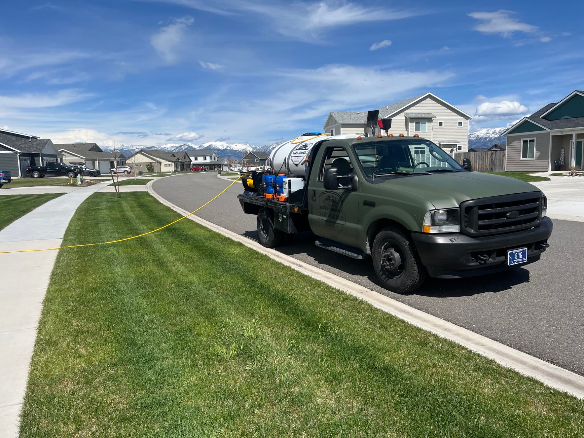 Yardguard service truck parked on a residential street with a Bozeman-area home and sky behind it