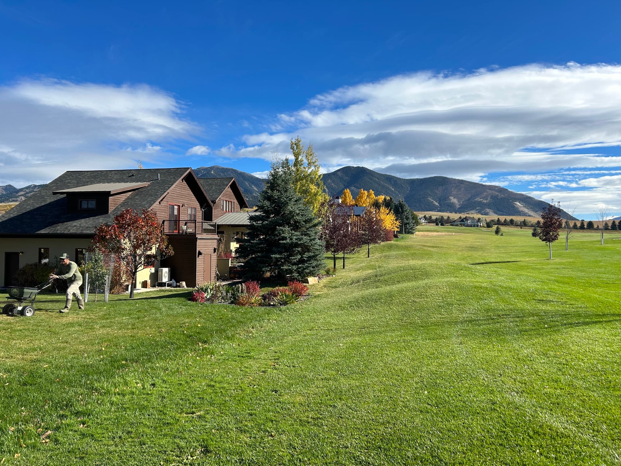 Lawn-care tech mowing a residential lawn with a Montana home and mountain backdrop